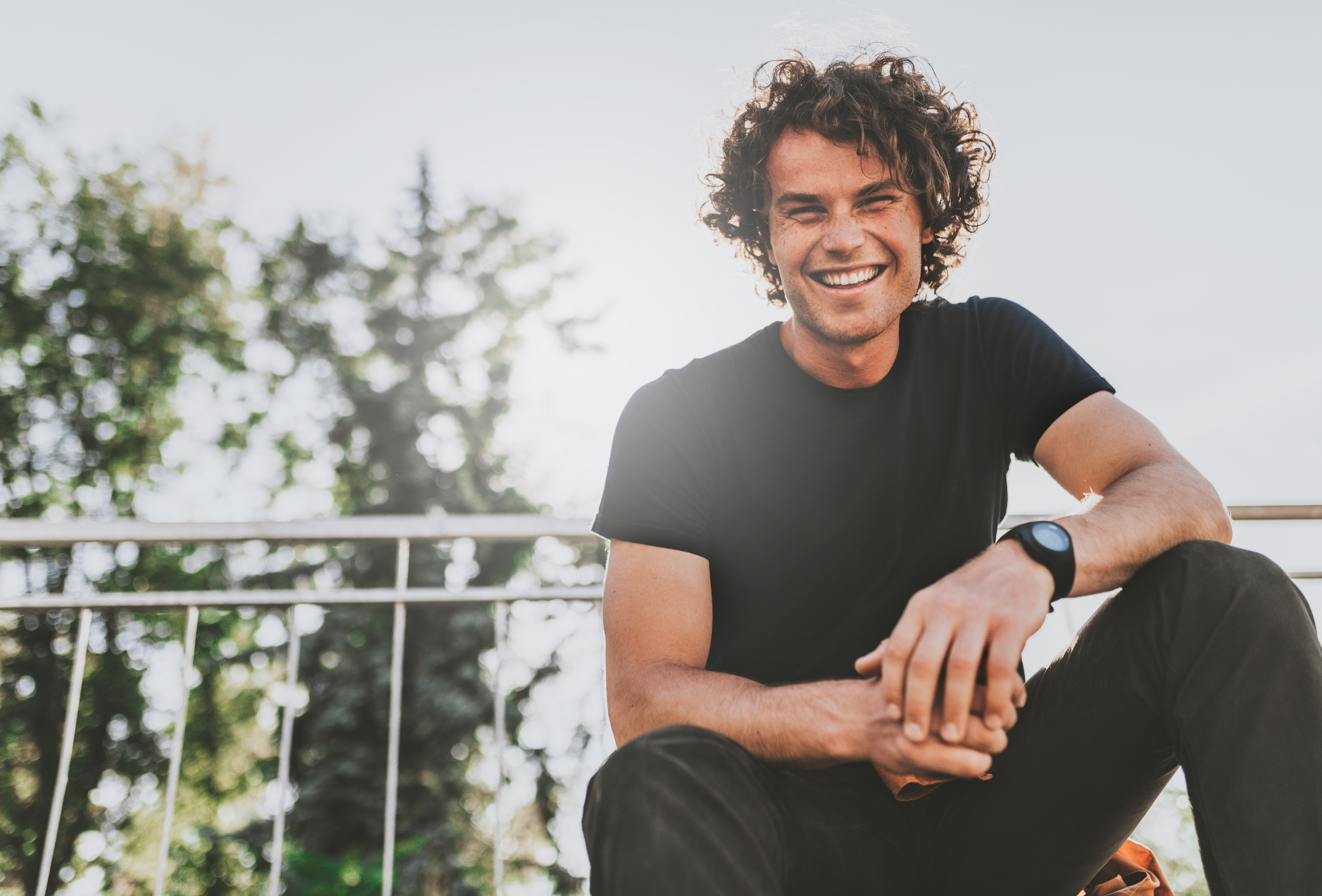 Low view shot of happy stylish young man wears black t-shirt and wirstwatch on the street. Happy smiling man posing for advertisement with copy space, outdoor in the city street. People concept Low view shot of happy stylish young man wears black t-shirt and wirstwatch on the street. Happy smiling man posing for advertisement with copy space, outdoor in the city street.